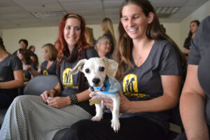 Image of two women wearing Remember Me Thursday shirts while holding a small white puppy.