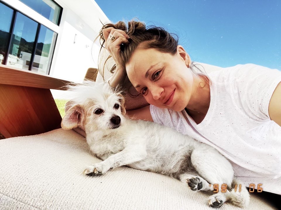 Kaley Cuoco laying down on her side right next to a fluffy small white dog.