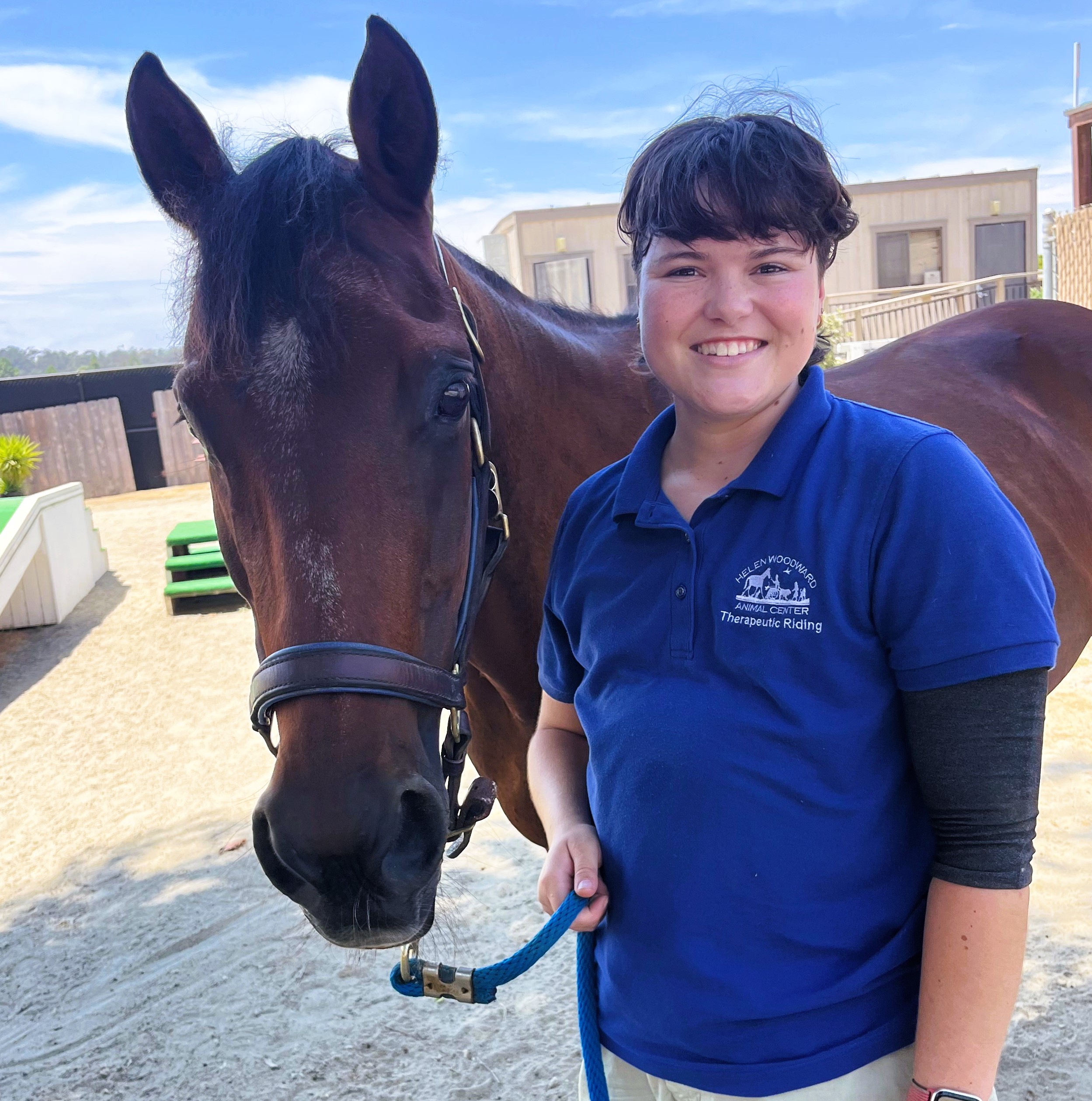 Pic of a brown horse next to a brunette staff member.