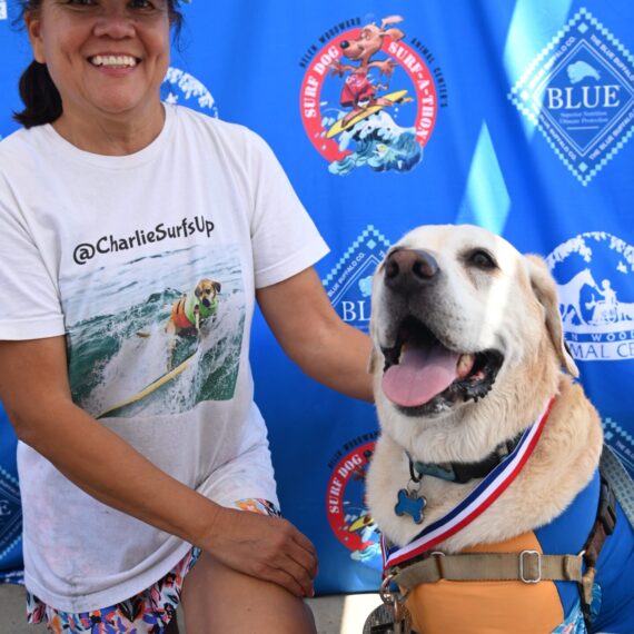 A woman smiling at the camera next to her white dog