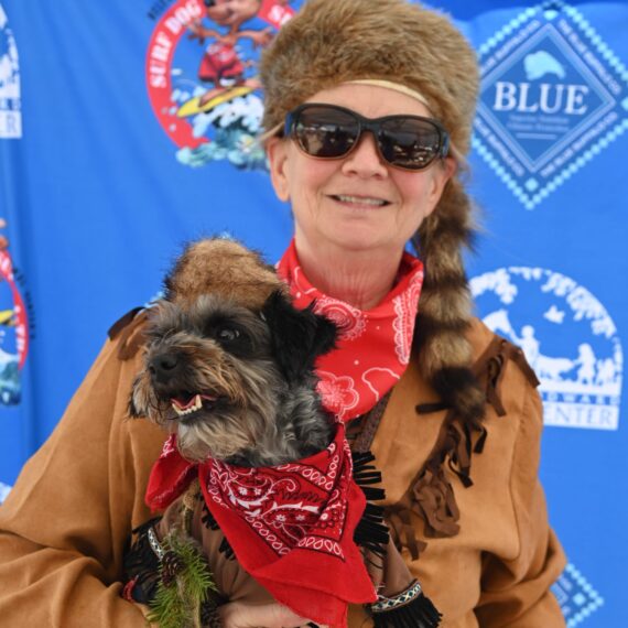 A woman with her black dog smiling at the camera