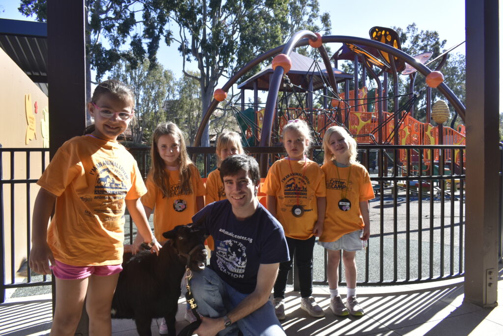 Kids and an instructor kneeling/standing around a goat
