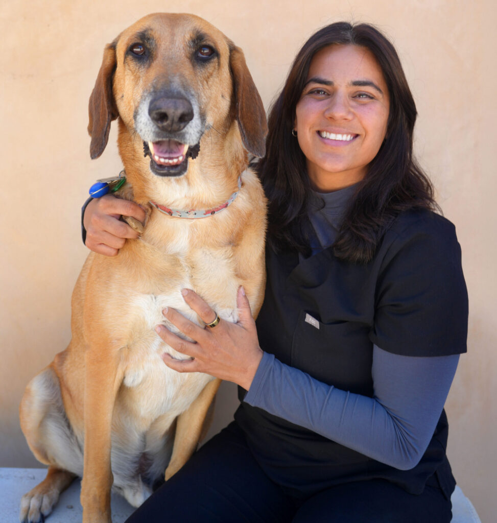Dr.Jannae Waney, a female doctor with dark hair, sitting next to her brown hound dog.
