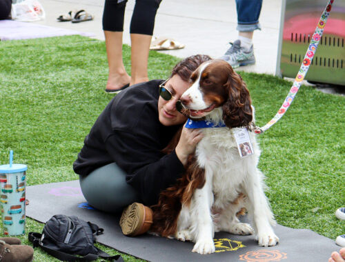 A man sitting outside, on a yoga mat hugging a therapy dog