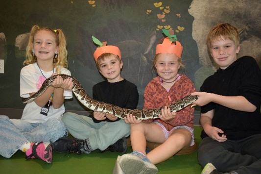 Children sitting on a floor holding a python snake
